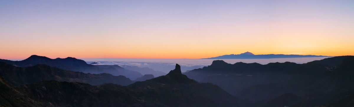 Dieses Panaroma entstand von einer der höchsten Erhebungen Gran Canarias. Es zeigt den alten Vulkanschlot Roque Bentaiga und umgebende Gebirge. Am Horizont erkennt man eine Wolkendecke, die über dem Atlantik liegt. Rechts ragt die Nachbarinsel Teneriffa mit dem größten Berg Spaniens, dem Teide, aus den Wolken.